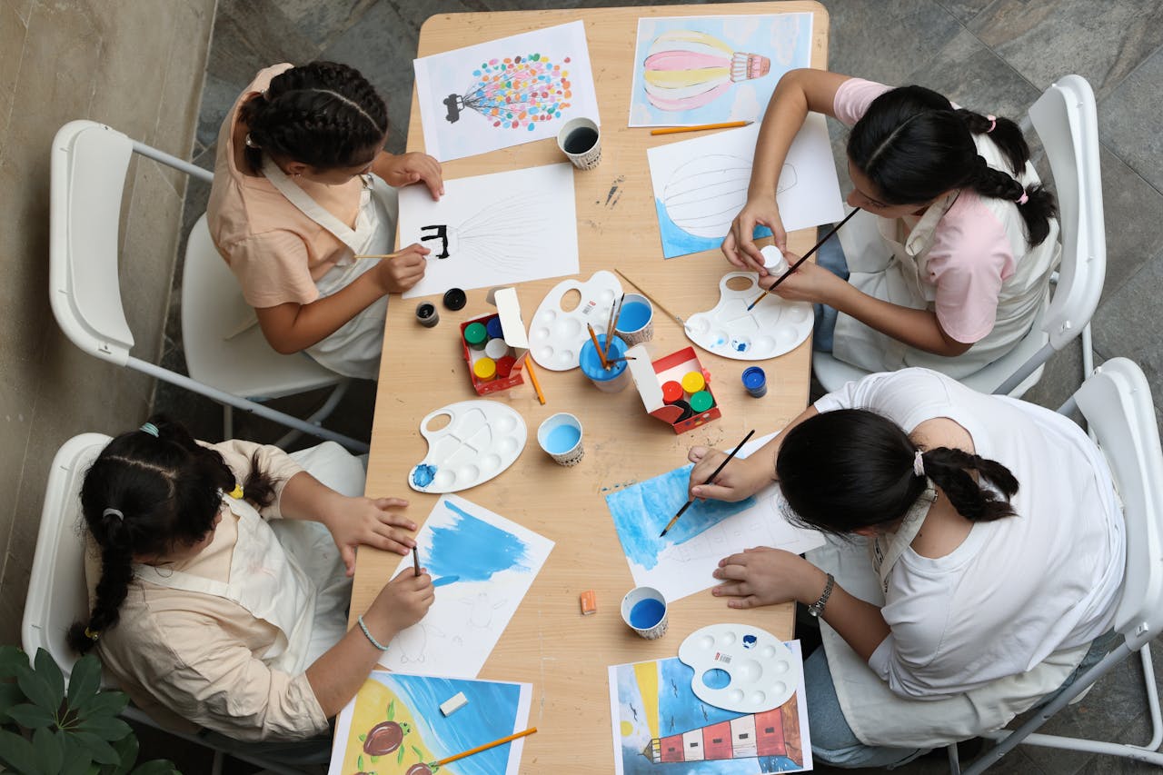 Five children engrossed in painting and drawing around a table, fostering creativity and learning.